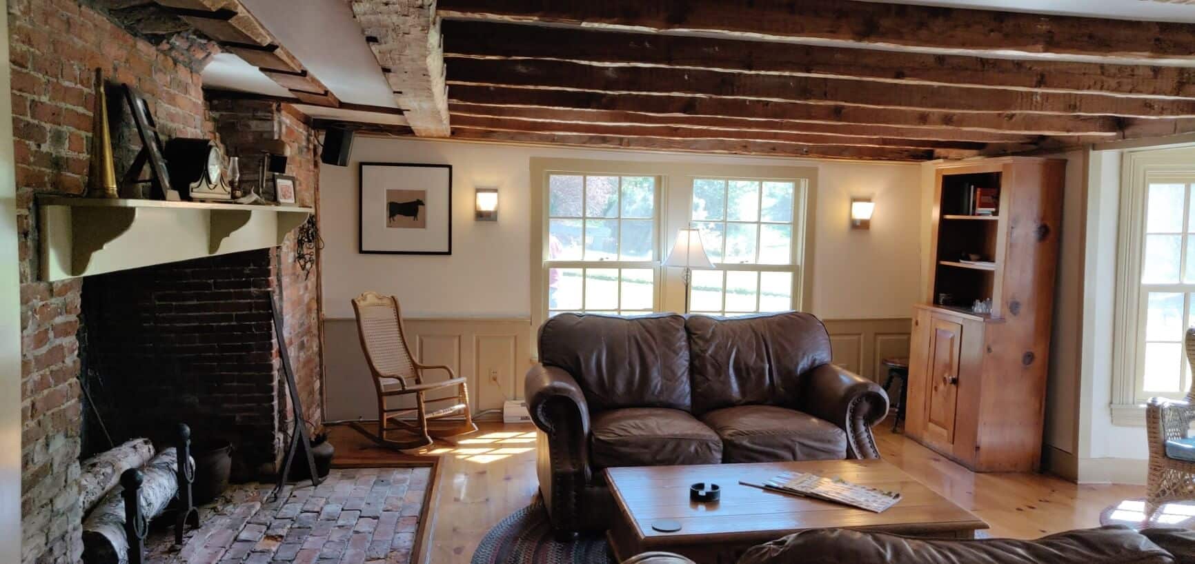 View of room with windows and leather love seats, a large brick fire place and exposed beams on ceiling