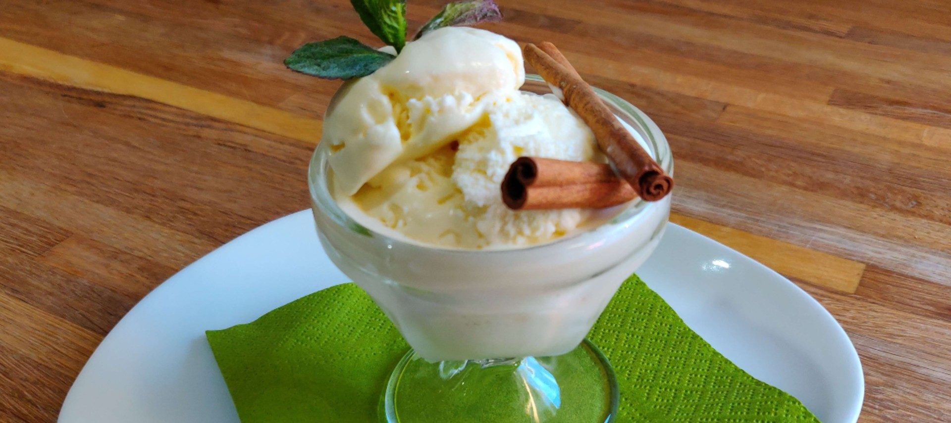 A bowl of ice cream garnished with cinnamon sticks and mint sprigs, on a white plate with a green napkin.