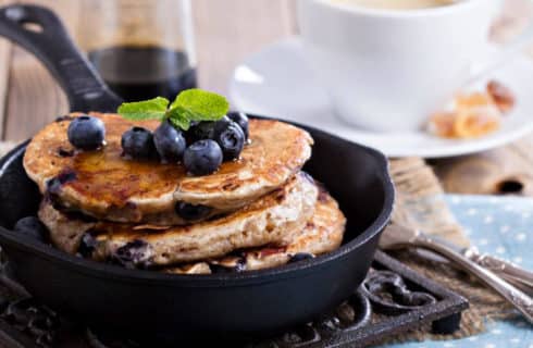 Cast-iron skillet with blueberry pancakes sitting on metal trivet on table set for breakfast