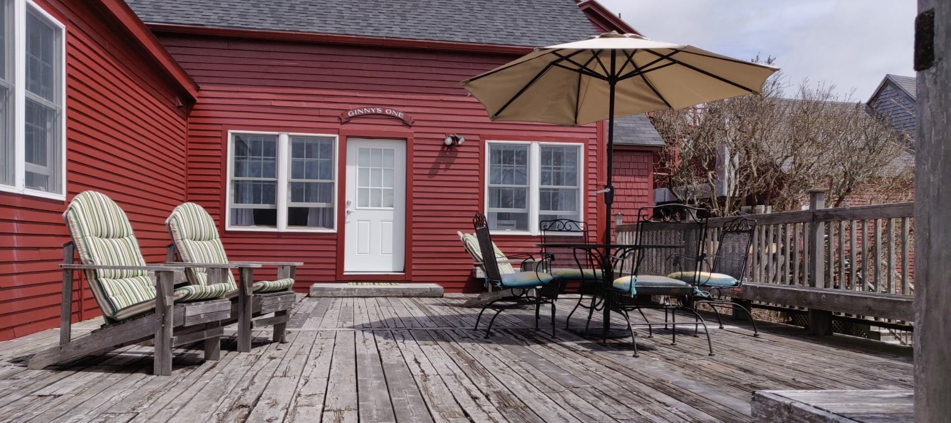 Large wooden deck with adirondack chairs, patio table, patio chairs, and patio umbrella