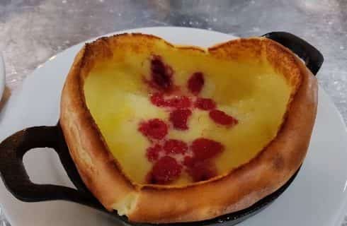 Mini dutch baby dessert shaped in a heart in small cast iron pan on white plate