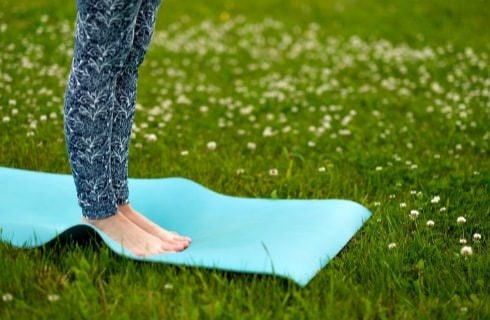 Close up view of a person's leggs with white and navy leggings standing on a light blue yoga mat in a field of green grass