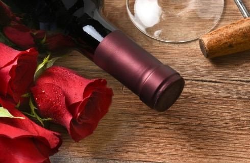 Close up view of red roses, top of wine bottle, bottom of wine glass, and bottle opener